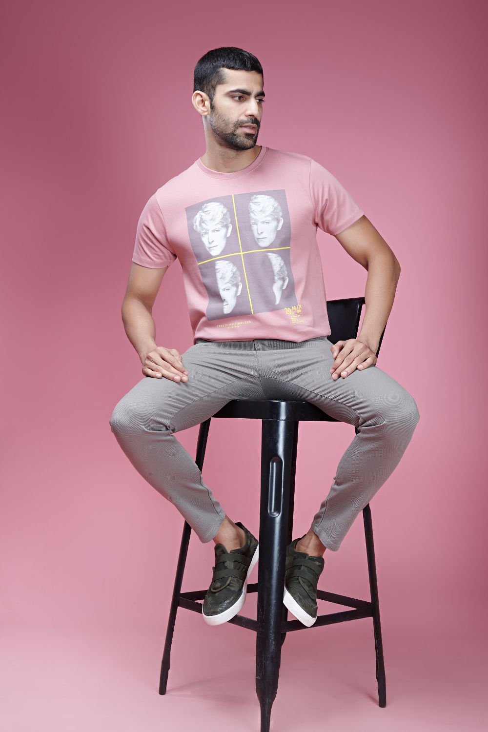 A model wearing Ash Rose colored, cotton Graphic T shirt for men, half sleeves and round neck.